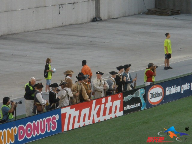 纽英兰的拉拉队员身着传统服装，手持老式前膛枪，分别站在两侧球门后方，为自己的球队加油助威。
